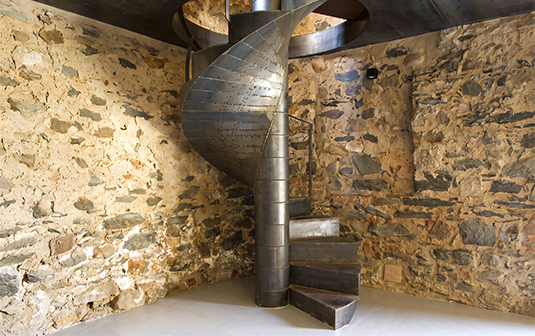 Escalier hélicoïdal métallique à fût central dans un intérieur en pierre